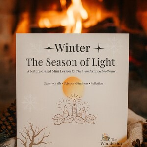 May include: A book titled "Winter The Season of Light" with illustrations of candles and a tree. The book is by The Wanderiny Schoolhouse. The background features a cozy fireplace and pinecones.