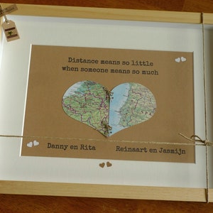 Könnte beinhalten: Ein gerahmter Druck mit braunem Hintergrund und einer ausgeschnittenen herzförmigen Karte. Die Karte ist in zwei Teile geteilt, mit dem Text "Distance means so little when someone means so much" darüber. Die Namen "Danny en Rita" und "Reinaart en Jasmijn" stehen unter der Karte.