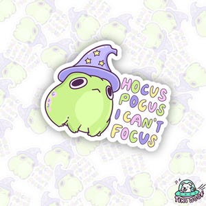 May include: A die-cut sticker featuring a light green cartoon creature wearing a purple wizard hat with gold stars. The sticker has the text "Hocus Pocus I Can't Focus" in colorful bubble letters. The sticker is from Tiki Woof.