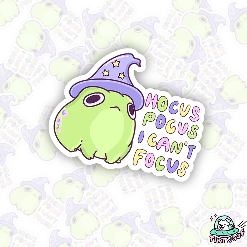 May include: A die-cut sticker featuring a light green cartoon creature wearing a purple wizard hat with gold stars. The sticker has the text "Hocus Pocus I Can't Focus" in colorful bubble letters. The sticker is from Tiki Woof.