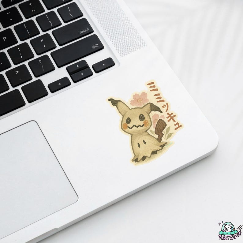K&ouml;nnte beinhalten: Ein Aufkleber mit einem Cartoon-Mimikyu-Charakter mit einem l&auml;chelnden Gesicht, braunen Ohren und einem kleinen Schwanz. Der Aufkleber hat japanischen Text und rosa Blumenakzente. Der Aufkleber befindet sich auf einem wei&szlig;en Laptop.