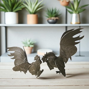 Könnte beinhalten: Zwei bronzefarbene Hahnen-Skulpturen stehen auf einer Holzoberfläche. Die Hähne stehen sich gegenüber, einer scheint sich gerade zu bewegen. Die Skulpturen weisen detaillierte Feder- und Kammdesigns auf und verleihen einen rustikalen Charme.