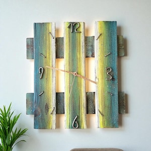 May include: A square wooden wall clock with a rustic design. The clock face is made of vertical wooden planks painted in shades of blue, green, and yellow. Metal numerals mark the hours. The clock hands are thin and brown.