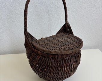 Vintage donkerbruine rieten wandmand met scharnierend deksel en gebogen handvat. Hangende organizer van rotan, cottagecore boho stijl, ideaal voor de hal of als brievenbak.