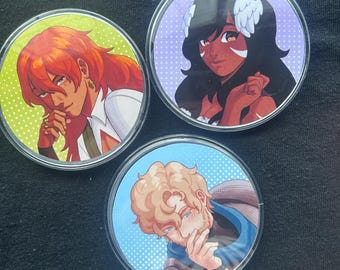 May include: Three circular buttons with clear backs, each displaying an anime-style illustration. One features a red-haired character on a green backdrop, another a dark-haired character on purple, and the third a blonde character on blue.