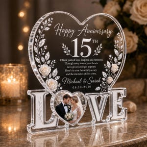 May include: A clear acrylic heart-shaped plaque featuring the text Happy Anniversary 15th, a poem, the names Michael & Sarah, and the date 06.18.2010. The plaque is decorated with white roses and crystal-like vines, resting on a base spelling LOVE.