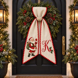 Può includere: Una ghirlanda natalizia con aghi di pino verdi, pigne e bacche rosse, decorata con un drappo in tessuto a righe beige e bianco. Il tessuto mostra un'illustrazione di Babbo Natale su un lato e una lettera K rossa sull'altro.
