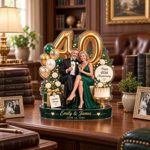 以下が含まれることがあります： 40周年記念のアクリル製ディスプレイ。シャンパングラスを持つカップル、金色の数字バルーン、緑と金のバルーン、白い花、Together Alwaysと書かれたギフトボックス、ケーキが飾られています。Emily & James, June 14, 1985と刻印されています。