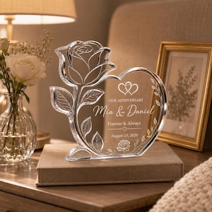 May include: A clear acrylic heart-shaped plaque featuring an etched rose design and the text: OUR ANNIVERSARY, Mia & Daniel, Forever & Always, August 15, 2020. The plaque includes two small heart icons and a small rose illustration at the bottom.