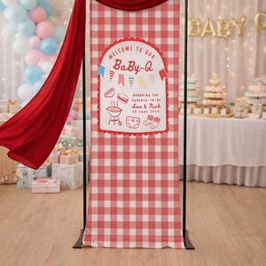 May include: A red and white chequered banner with the text "WELCOME TO OUR BaBy-Q" is displayed at a baby shower. The banner includes illustrations of food and baby items. A red fabric drapes from the top.