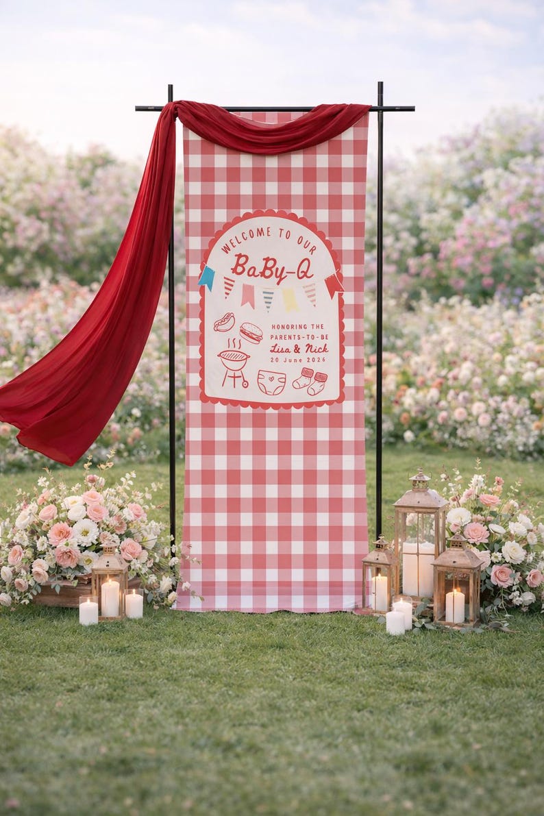May include: A red and white gingham banner with the text "WELCOME TO OUR BaBy-Q" is displayed at an outdoor event. The banner includes illustrations of a grill, hot dog, burger, diaper, and socks. A red fabric drapes from the top. Lanterns and flowers are in the foreground.
