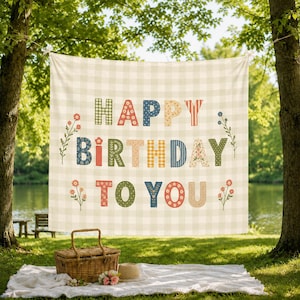 May include: A square fabric banner featuring a light green and white gingham pattern with the text HAPPY BIRTHDAY TO YOU in multi-colored, patterned block letters. The design includes small floral illustrations on the sides of the text.