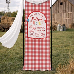 May include: A red and white chequered Baby-Q banner with the text "WELCOME TO OUR BaBy-Q" and "HONORING THE PARENTS-TO-BE Lisa & Nick 20 June 2026". The banner is displayed outdoors with a white drape.
