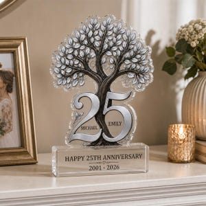 May include: A clear acrylic commemorative plaque featuring a detailed tree design with silver-toned leaves. The large number 25 is integrated into the trunk, with the names Michael and Emily engraved. The base reads HAPPY 25TH ANNIVERSARY 2001-2026.