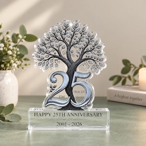 Pode incluir: Uma placa de acrílico transparente com uma ilustração detalhada de uma árvore e um grande número 25 prateado integrado no tronco. A base está gravada com HAPPY 25TH ANNIVERSARY, 2001-2026 e os nomes TIM e TRACEY.