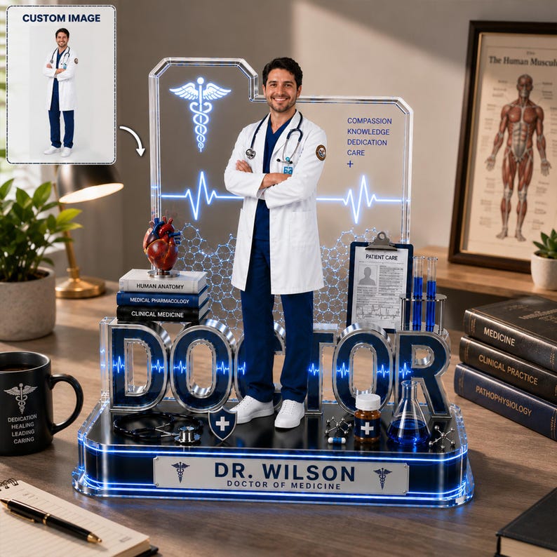 Puede incluir: Un adorno de escritorio de m&eacute;dico personalizado con una figura masculina con bata blanca, con la palabra "DOCTOR" en letras grandes. La base incluye el nombre del m&eacute;dico y s&iacute;mbolos m&eacute;dicos. Elementos adicionales incluyen libros de medicina, un modelo de coraz&oacute;n y tubos de ensayo.