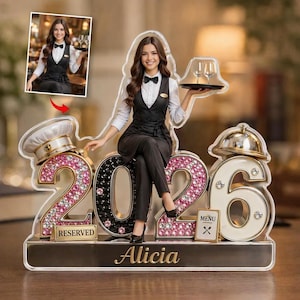 May include: A decorative acrylic figure featuring a woman in a server uniform, seated on the numbers "2026". The "2" and "6" are embellished with pink and white rhinestones. The base reads "Alicia" and "Reserved".