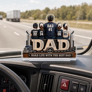 May include: A clear acrylic dashboard ornament featuring a design for a truck driver. The ornament has the word "DAD" in large letters, with the text "ROAD LIFE WITH THE BEST DAD" below. It includes figures of a father and children with names and numbers.