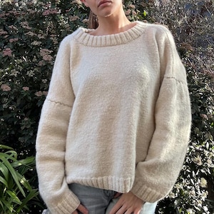 Può includere: Un maglione color crema con scollo tondo e maniche lunghe. Il maglione presenta un design a maglia strutturata e dettagli a coste su scollatura, polsini e orlo. Le maniche hanno una leggera forma a palloncino. Il maglione è realizzato in un materiale morbido e caldo.