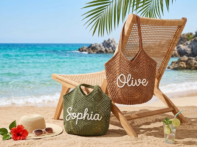 May include: A beach scene with a woven chair, two crochet tote bags, a straw hat, and a cocktail. One bag is brown with "Olive" in white, the other is green with "Sophia". The hat has sunglasses. A red hibiscus flower is on the sand.