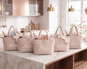May include: Five quilted blush pink tote bags with two handles each, featuring white embroidered names Chloe, Ava, Mia, Sophie, and Zoe. Each bag contains various gift items including small bottles, wrapped boxes, and sleep masks.