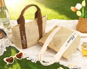 May include: Two woven straw tote bags with brown and cream accents, personalized with the names "Clara" and "Olivia". The bags are on a white blanket with heart-shaped sunglasses and a bottle of champagne.