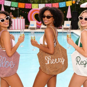 May include: Three women holding champagne flutes and wearing sunglasses pose by a pool. Each woman carries a woven tote bag with a name embroidered on it: Chloe, Sherry, and Regina. The bags are in pink, brown, and white.