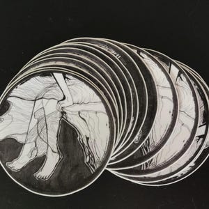 May include: A stack of round stickers featuring a black and white illustration of a person's legs and flowing fabric. The artwork is detailed with fine lines and shading, creating a sense of movement and depth. The stickers are arranged on a black surface.