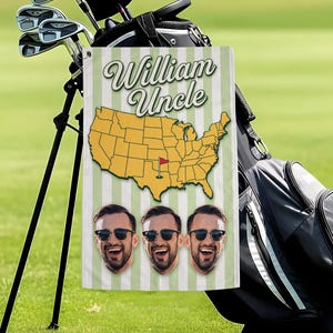 May include: A golf towel with a green and white striped background, featuring the text "William Uncle", a yellow map of the USA with a red flag, and three smiling faces. The towel is hanging on a golf bag.