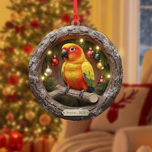 May include: A round Christmas ornament featuring a colorful parrot perched on a branch within a wooden frame. The parrot has yellow, orange, and green feathers. The frame is decorated with small lights, ornaments, and the text "Jessica - 2025".