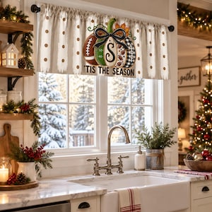 May include: A window valance featuring a beige background with brown polka dots and vertical brushstrokes. The center displays a large pumpkin graphic with football-themed segments, a black bow, and the text 'TIS THE SEASON' in black lettering.