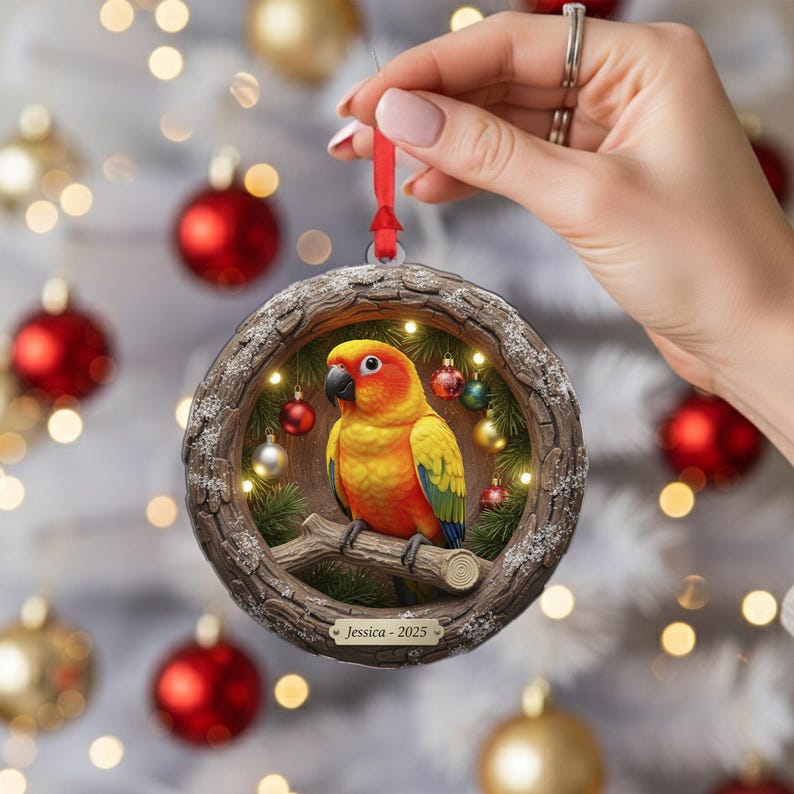 May include: A round Christmas ornament featuring a vibrant yellow, orange, and green parrot perched on a branch. The ornament is framed by a wooden-like border with small lights and miniature ornaments. The text "Jessica - 2025" is displayed on a small plaque.