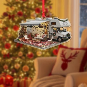 May include: A Christmas ornament shaped like a motorhome with a festive outdoor living space. The ornament features a decorated Christmas tree, a rug, and a sofa. The motorhome has the name "DAVID" on the front.