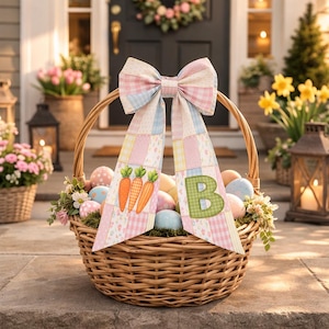 Puede incluir: Una cesta de mimbre tejida llena de huevos de Pascua decorados, flores y vegetación. Un gran lazo con cintas de patchwork pastel y aplicaciones de zanahorias y la letra "B" adorna la cesta, creando una exhibición primaveral festiva.