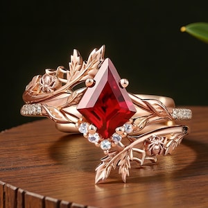 May include: A rose gold ring set with a large, faceted, red gemstone. The ring is decorated with leaf and floral details, and small, clear accent stones. The band has a delicate, nature-inspired design.