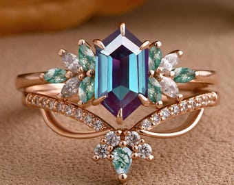 May include: A rose gold ring set featuring a central, hexagonal, teal and purple gemstone. The main ring is flanked by smaller green and white gemstones. A second ring with a curved design and small clear stones is included.
