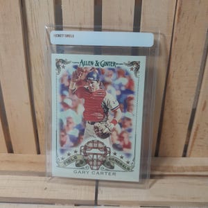 May include: A baseball card featuring Gary Carter from the 2020 Topps Allen & Ginter series. The card is encased in a Beckett Shield holder. The card has a vintage design with a portrait of Carter in his baseball uniform. The words "Field Generals" are also visible.