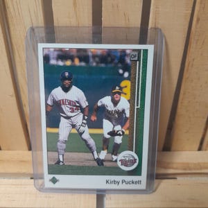 Puede incluir: Una taza de cerámica blanca con un asa negra y el texto "But First, Coffee" en negrita negra. La taza se encuentra sobre un fondo borroso, sugiriendo un ambiente acogedor.