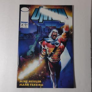 Puede incluir: Una portada de cómic que presenta a un superhéroe con un traje rojo y dorado con una capa, sosteniendo una espada brillante. La portada es azul y morada con un horizonte de ciudad en el fondo. El título del cómic es "Unknown" y el número de la edición es 2. El cómic es publicado por Image Comics.
