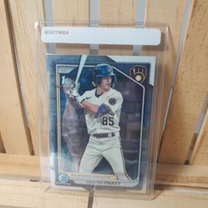 Puede incluir: Una tarjeta de béisbol con Cooper Pratt, un jugador de los Milwaukee Brewers. La tarjeta es una tarjeta cromada azul y dorada con una imagen de Pratt bateando. El número de la tarjeta es 85.