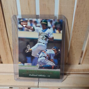 May include: A baseball card featuring a baseball player in a green and white uniform with the number 24 on the front. The player is in mid-air, sliding into home plate. The card is from the Upper Deck brand and features the player's name, Ricky Henderson, and the team, Oakland Athletics.