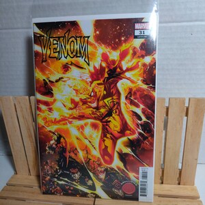 Könnte beinhalten: Venom #31 Comic-Cover mit einem feurigen roten und gelben Bild von Venom mit dem Text "VENOM" in großen Buchstaben oben und "MARVEL" und "31" in kleineren Buchstaben oben rechts.