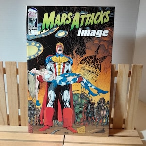 Puede incluir: Una portada de cómic con un superhéroe con un traje rojo, blanco y azul que lleva a una mujer con un traje similar. La portada se titula "Mars Attacks" con la palabra "image" debajo. El fondo presenta un edificio en llamas y platillos voladores.