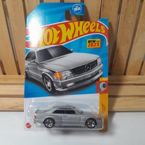 May include: A silver Hot Wheels die-cast model of a Mercedes-Benz coupe, packaged on a blue and yellow card. The card features the Hot Wheels logo and the text "NEW FOR 2023". The car is a 4/5 model.