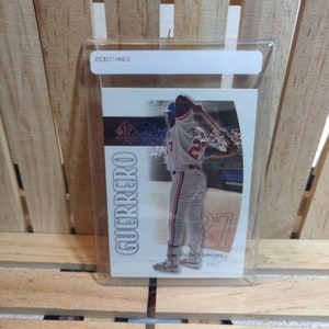 May include: A baseball trading card of Vladimir Guerrero in a batting stance, wearing a gray and blue uniform with the number 27. The card is in a protective holder, with the text "BECKETT SHIELD" visible.