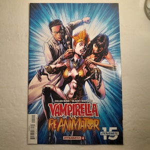 Może przedstawiać: Okładka komiksu z tytułem "Vampirella vs Reanimator". Grafika przedstawia dynamiczną scenę z trzema postaciami w żywej palecie barw. Projekt okładki sugeruje historię akcji i konfliktu.