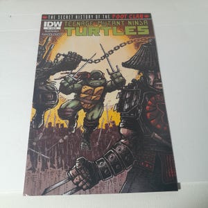 May include: A comic book cover for "Teenage Mutant Ninja Turtles" features a green turtle character wielding swords, with other figures in the background. The title text is in green and yellow. The cover has a dark, action-packed illustration.