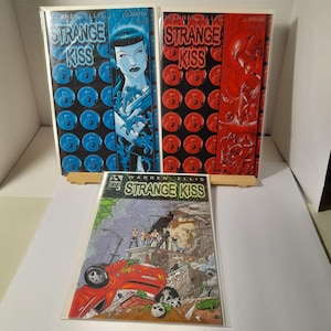 May include: Three comic books with the title "Strange Kiss" by Warren Ellis. The covers are blue, red, and green with illustrations of characters.
