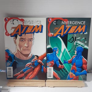 May include: Two comic books titled "Convergence The Atom" are displayed. Issue #1 features a man's face and a superhero. Issue #2 shows two superheroes facing each other. The covers are predominantly blue, orange, and white.