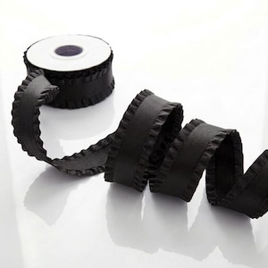 May include: A roll of black ribbon with a ruffled edge. The ribbon is unspooled, revealing its texture and design. The spool is white with a dark center.